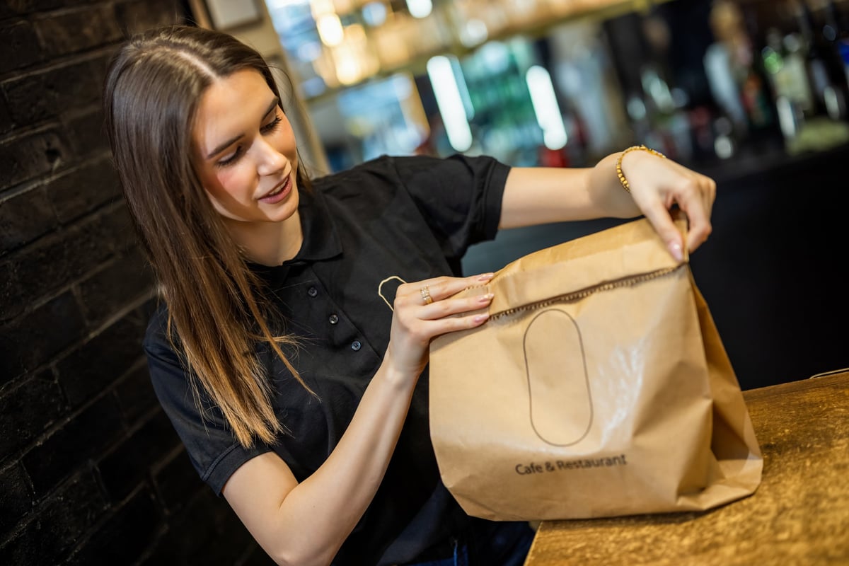 Team member carefully packing a takeaway meal into a paper bag